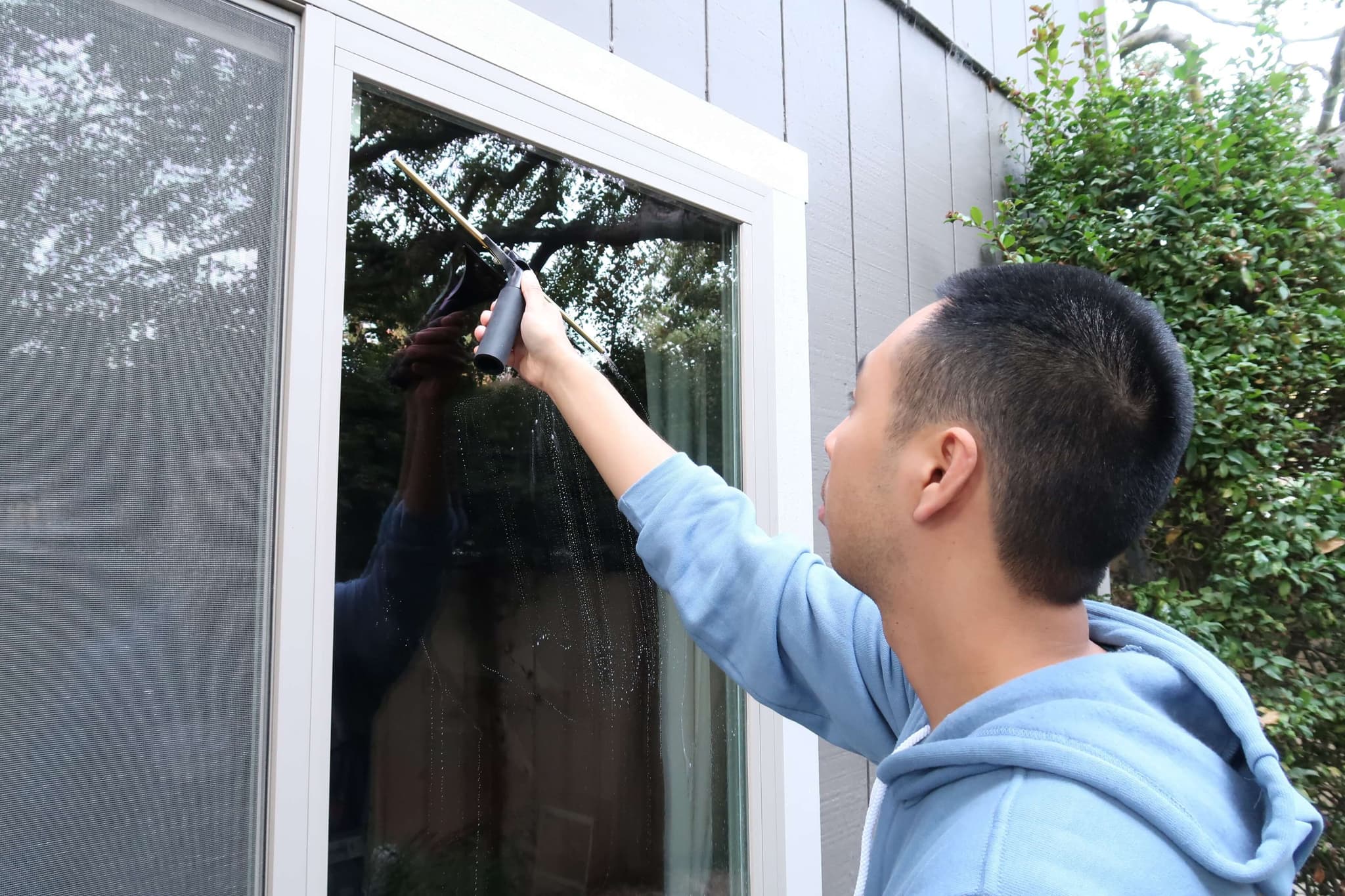 Technician squeegeeing a white trimmed window on a painted wood sided house