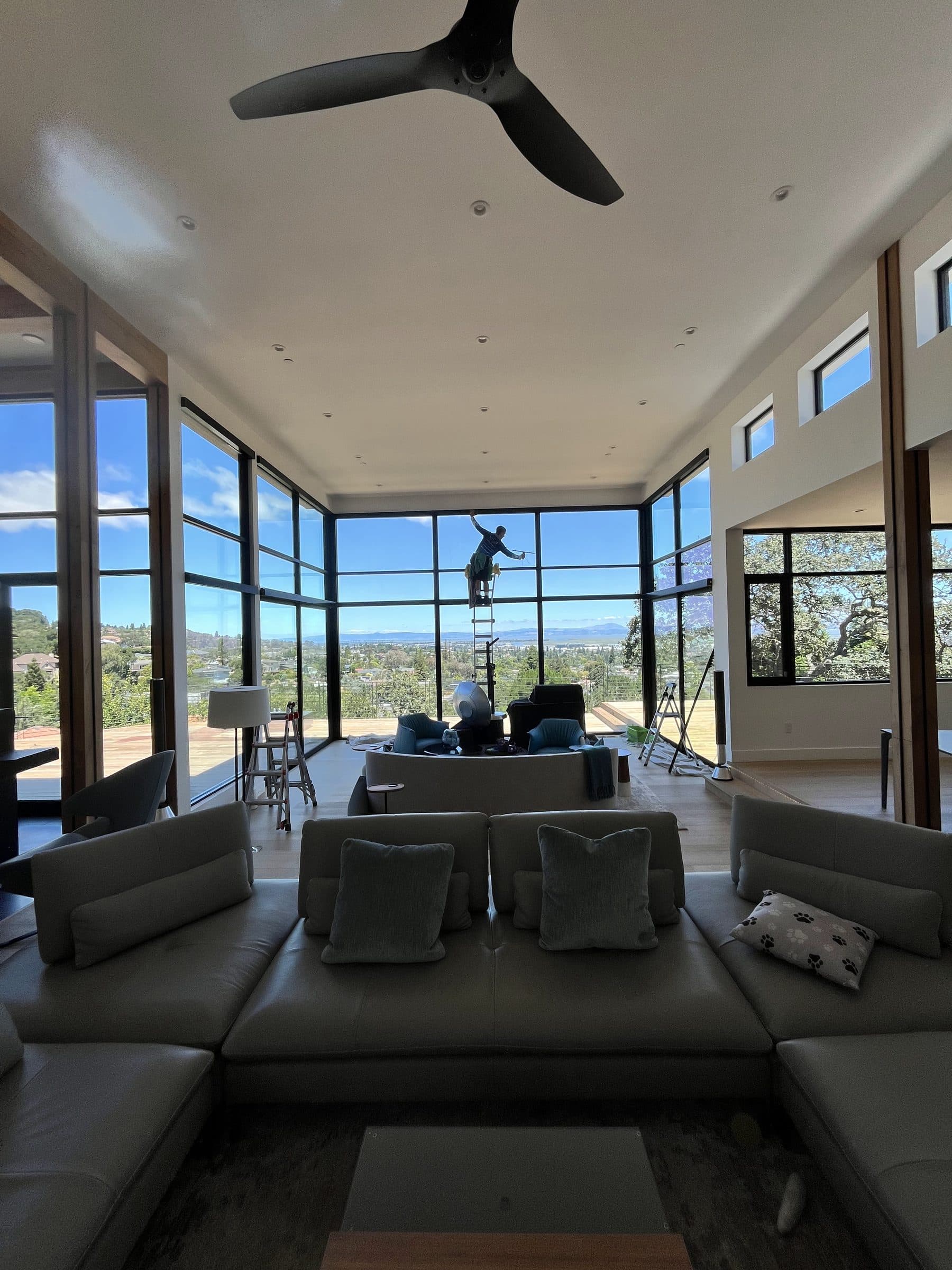 Living room with walls of glass looking out to the Bay while a technician cleans the exterior
