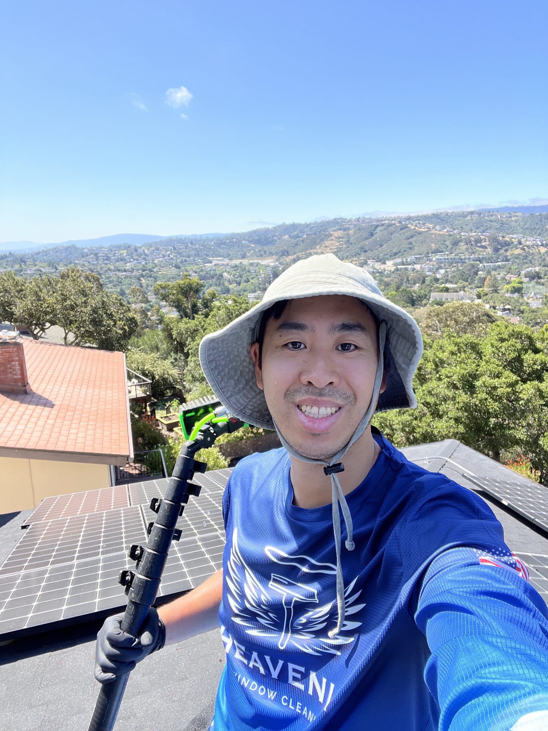 Heavenly technician with a water fed pole on a rooftop above a hillside neighbourhood