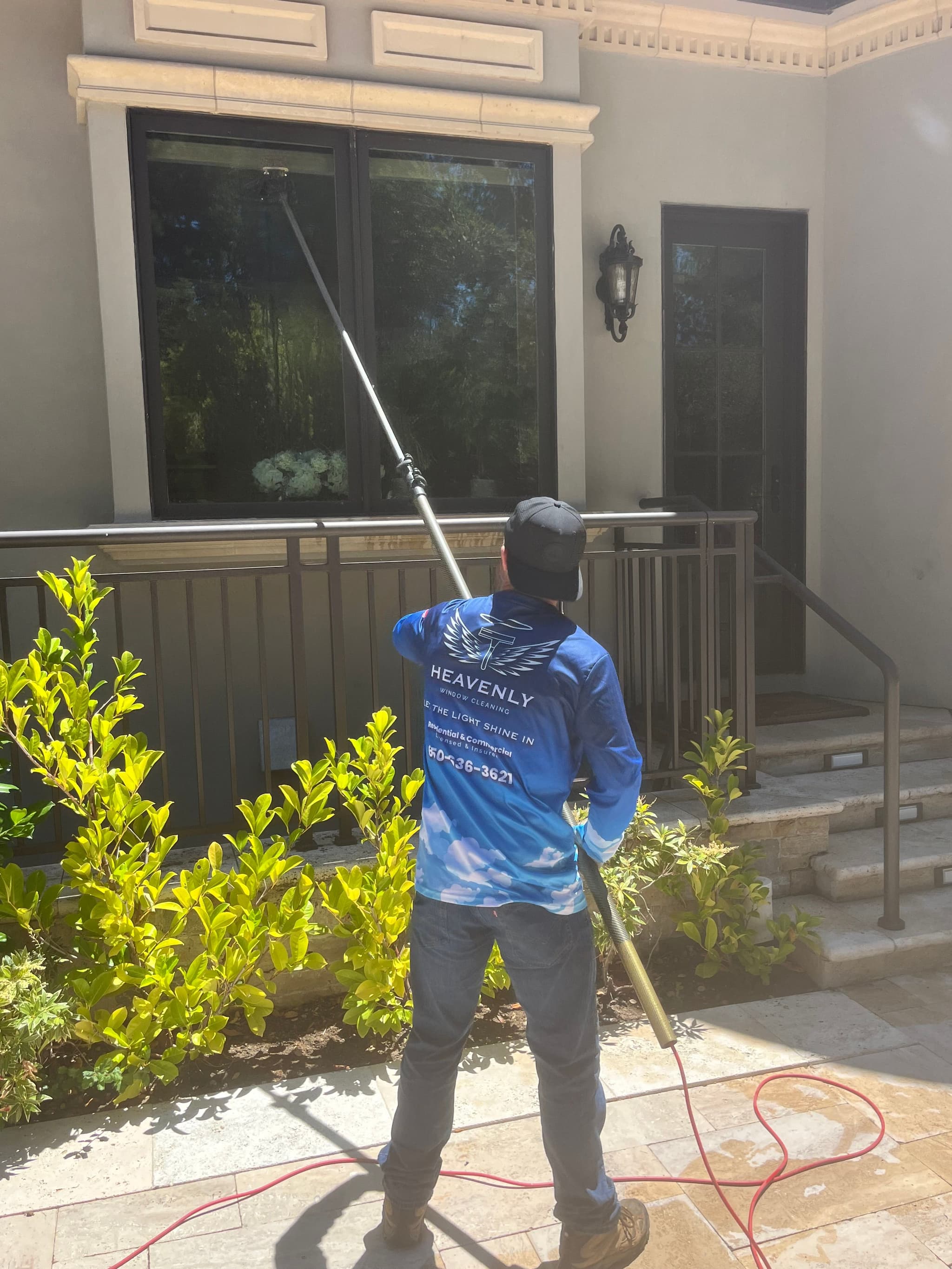 Technician reaching an upper storey window from the ground with a water fed pole