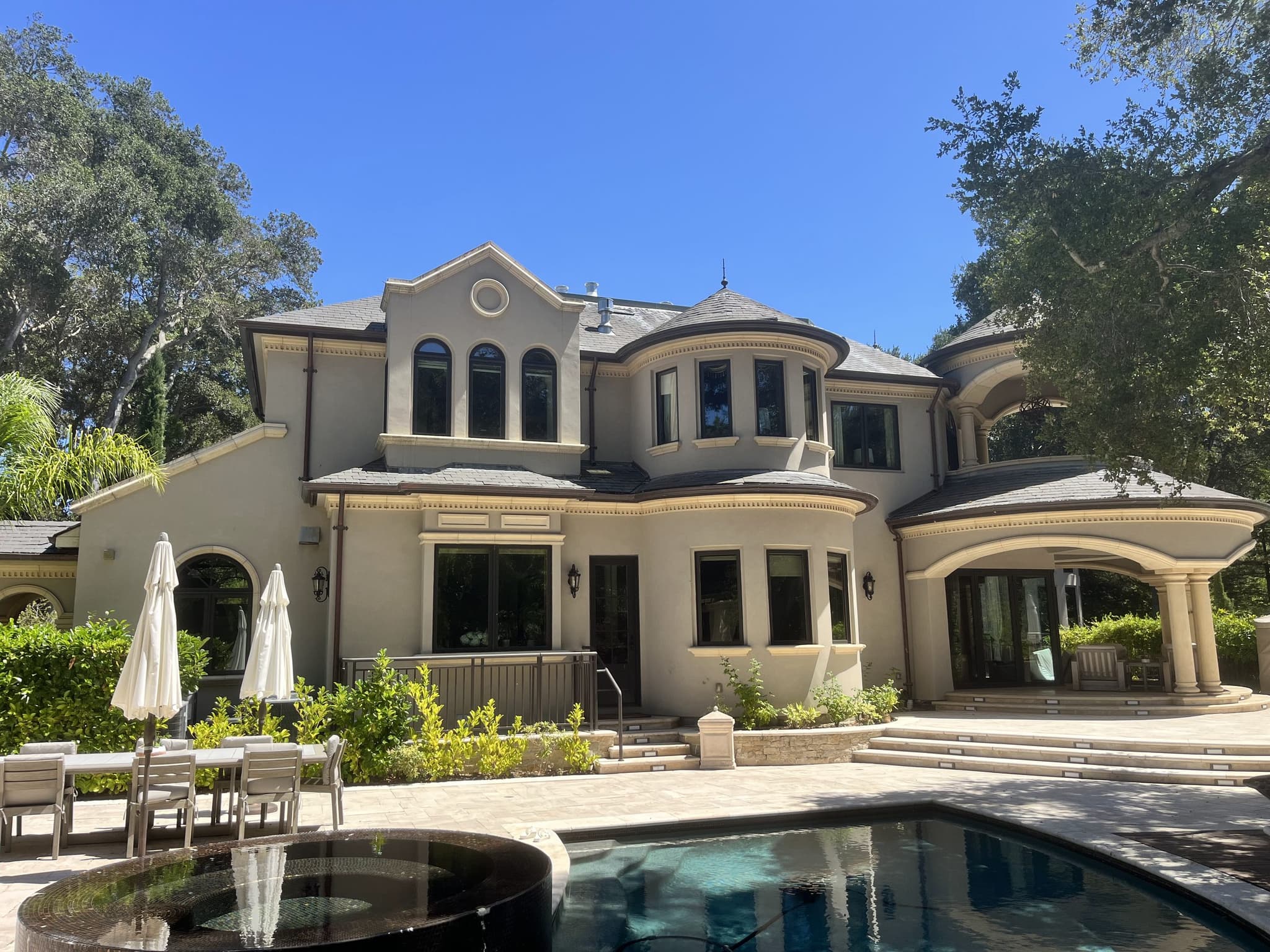 Large Mediterranean style home with arched windows behind a pool terrace